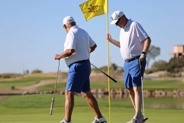 Two golfers tending the yellow pin flag on the green