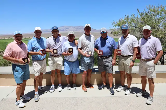 Eight golfers on the clubhouse patio holding award plaques with the desert course and mountains behind them